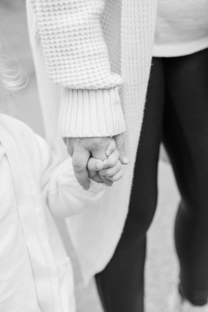 Close-up of a mother and child holding hands during an outdoor family picture session in Minnesota, captured in black and white.