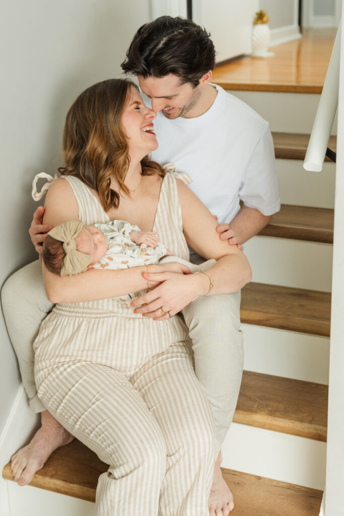 Parents sitting on stairs holding newborn baby girl during cozy in home newborn photography session in Minnesota.
