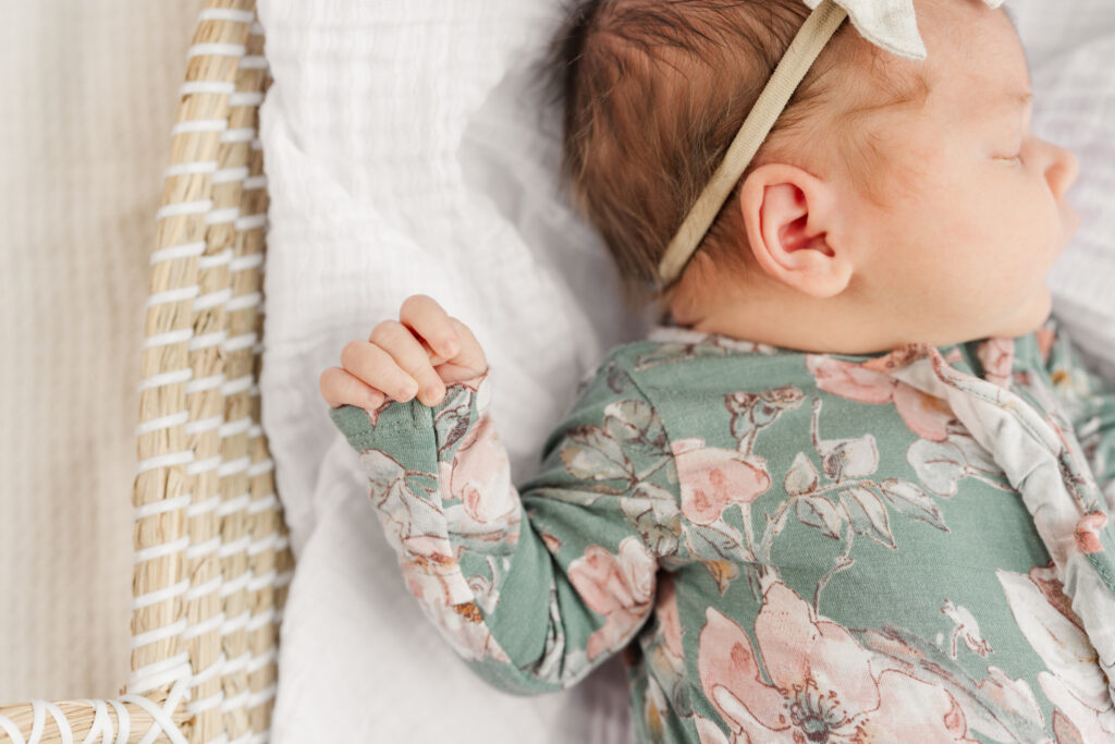Newborn baby girl sleeping in floral outfit during in home newborn photography session in natural light.