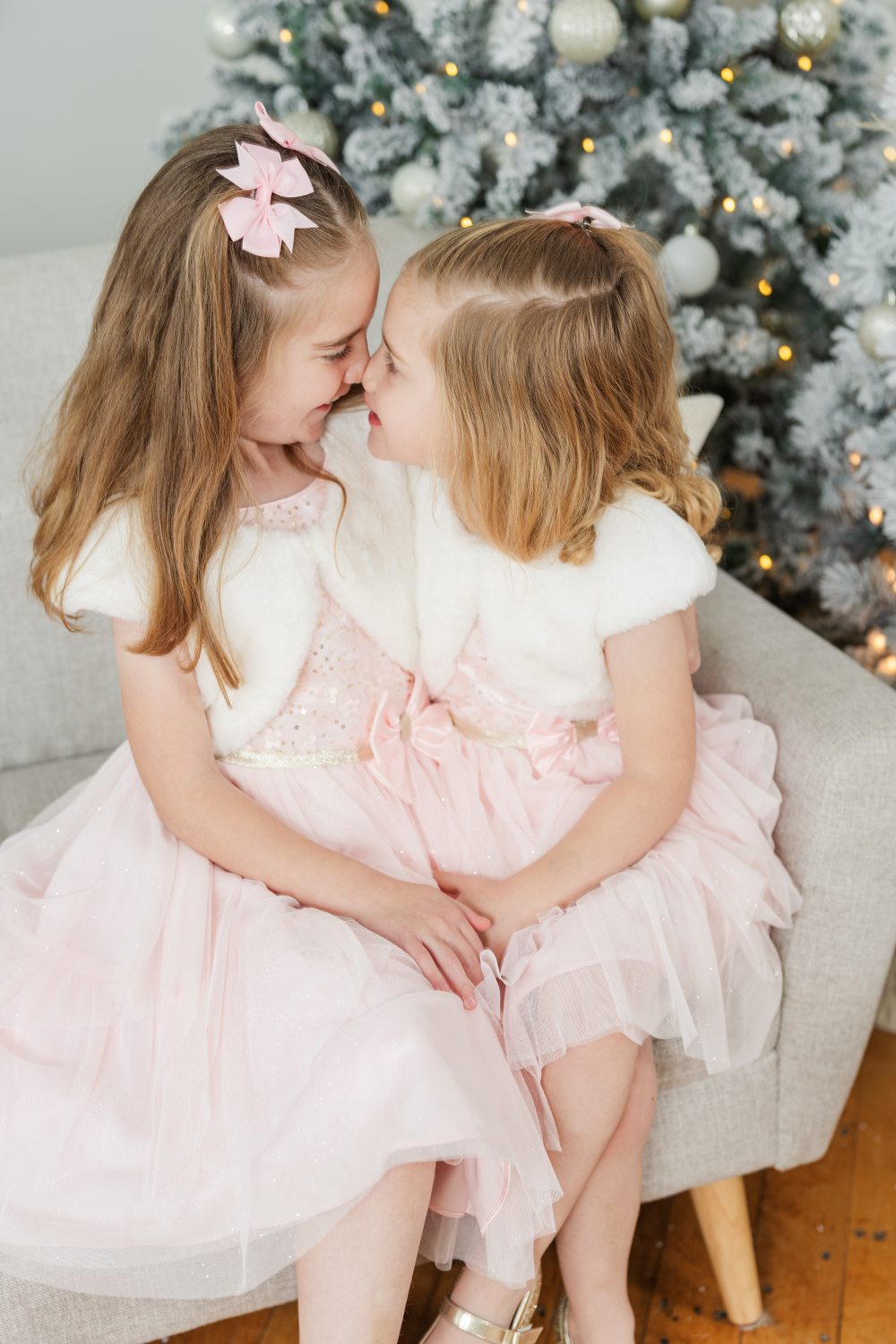 Sisters in matching pink dresses sharing a sweet moment during professional Santa photos in Minneapolis holiday studio.