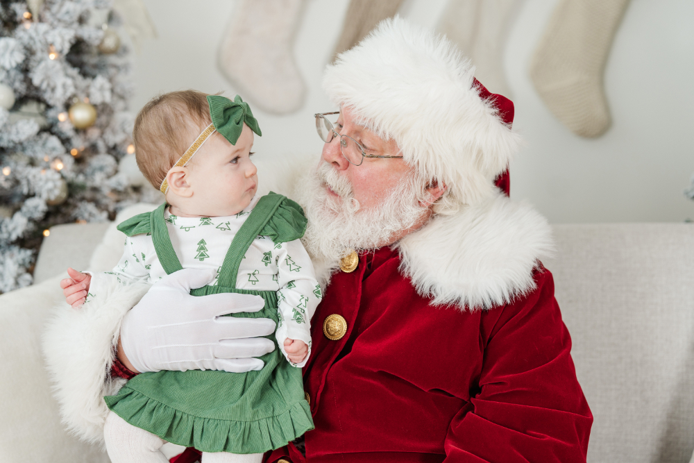 Santa holding a baby dressed in green as they share a sweet moment in a festive holiday studio setting.
