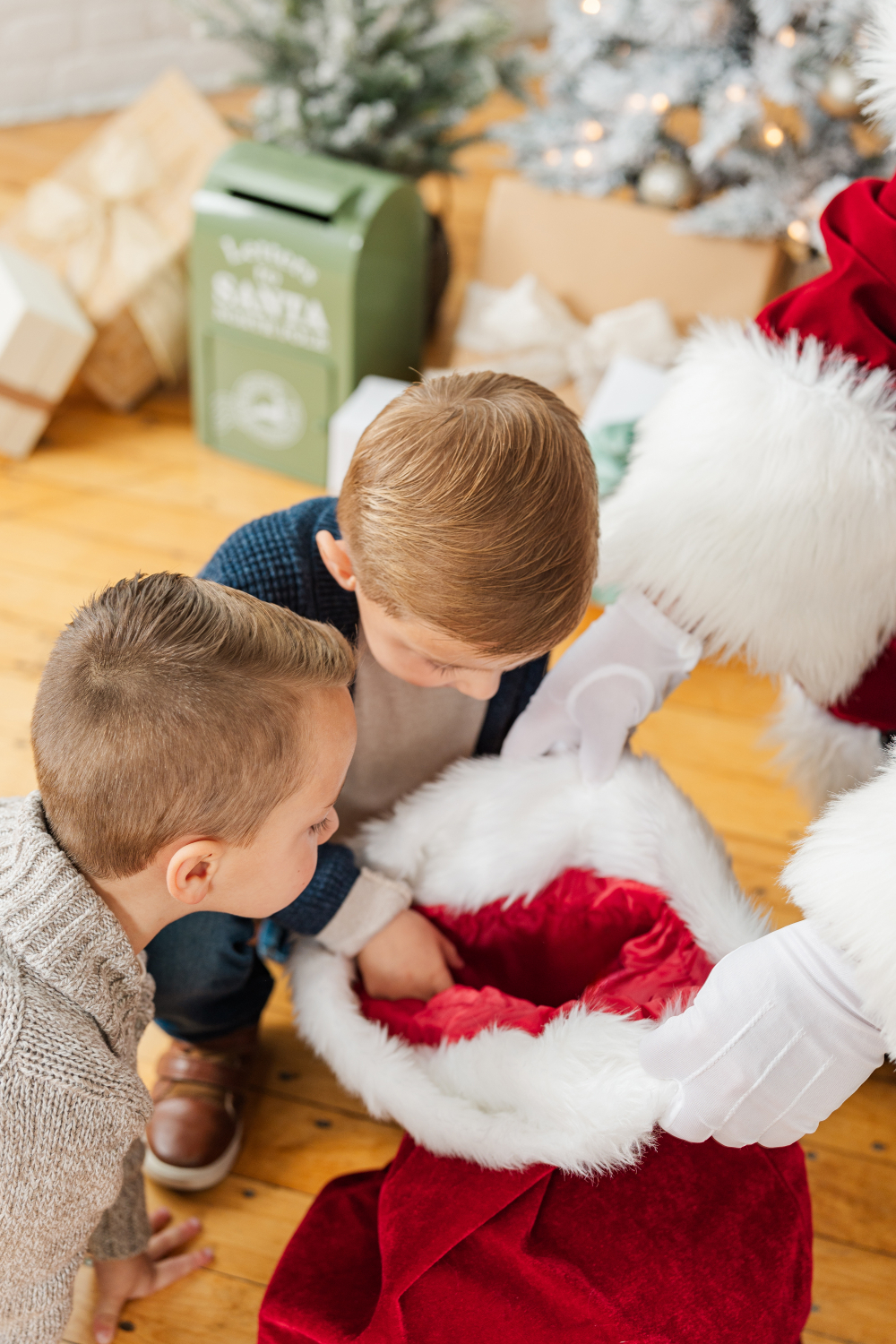 Children peeking into Santa’s gift bag during professional Santa photos in Minneapolis holiday studio with presents.