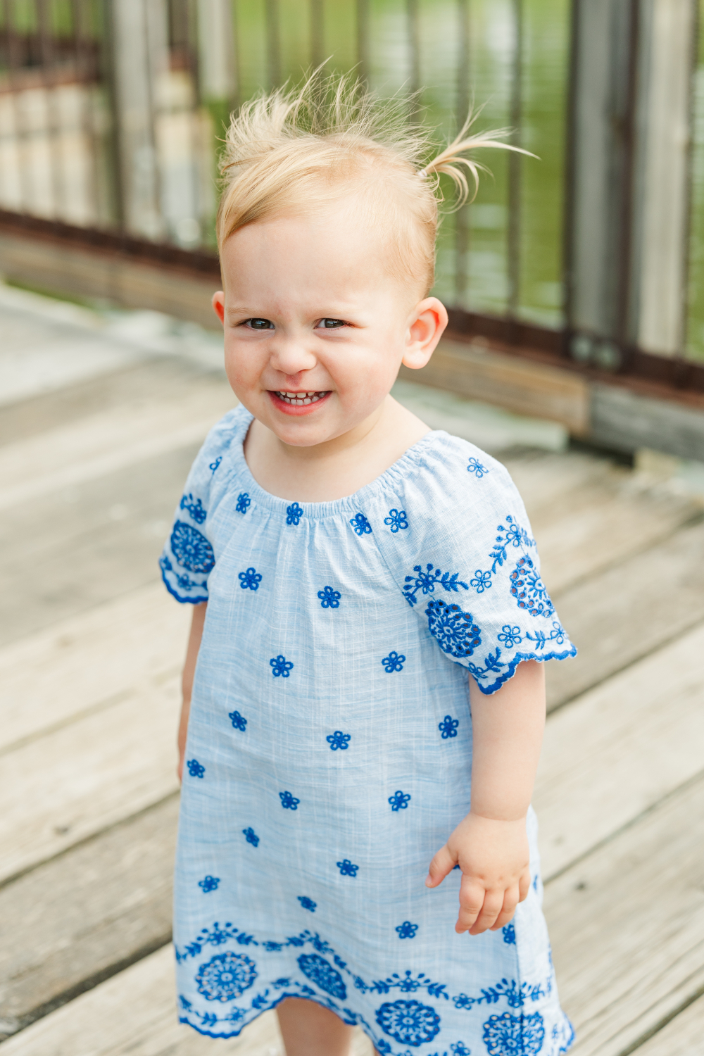 Smiling toddler in embroidered blue dress on a dock, a joyful way to turn family photos into heirlooms.