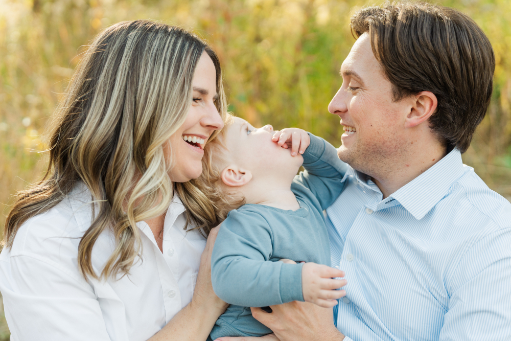 Smiling parents with toddler at golden hour, a joyful moment to turn family photos into heirlooms.
