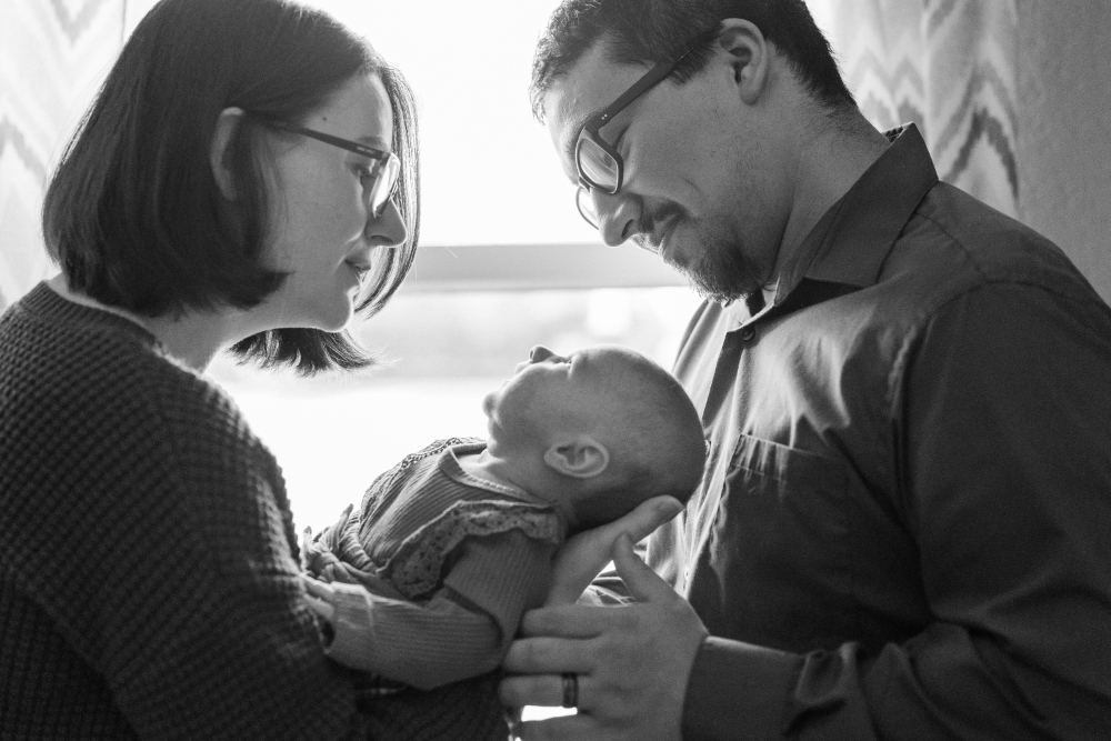 New parents gazing at their newborn in soft window light, a tender way to turn family photos into heirlooms.