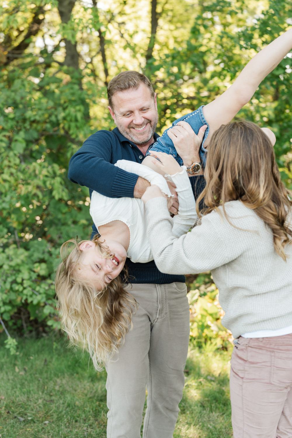 Father and mother playfully holding laughing daughter outdoors, a playful moment while photographing family.