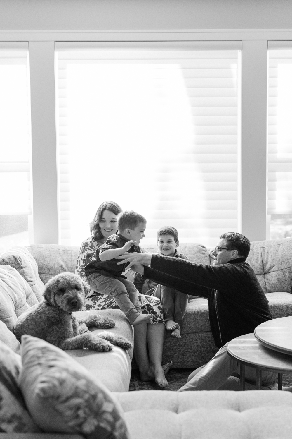Family laughing together on the couch with their dog nearby, sharing a cozy and joyful moment at home.
