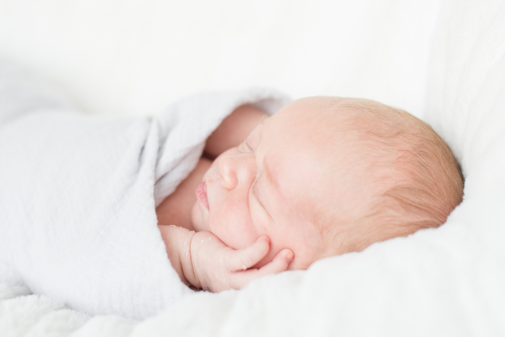 Newborn baby peacefully sleeping on a white blanket, wrapped in soft swaddle for booking a newborn session.