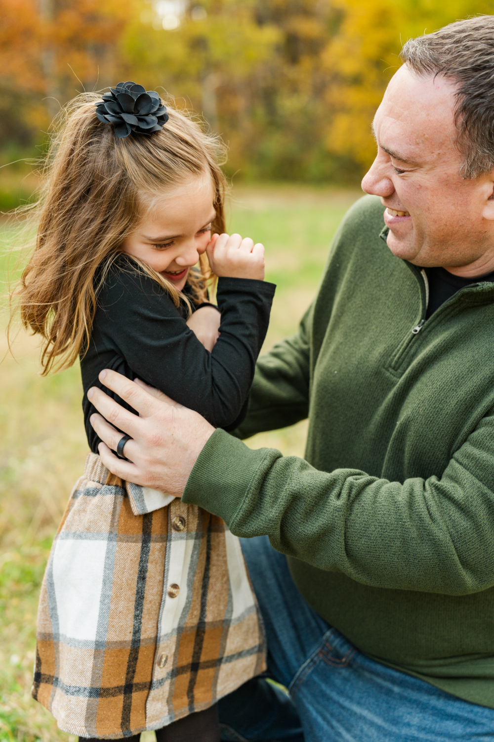 Father laughing while holding daughter outdoors during playful family photo session.