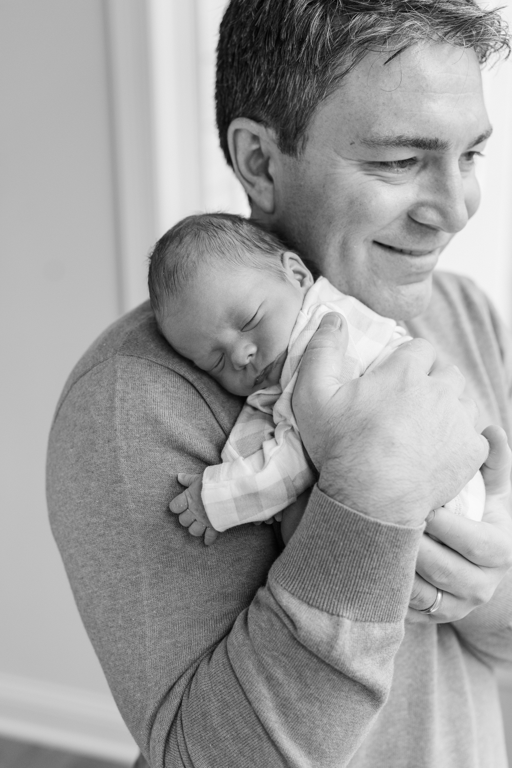 Minnesota newborn photographer captures proud father smiling while holding peacefully sleeping newborn against his shoulder.