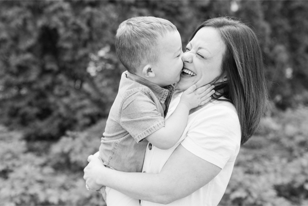 Photos I never want to live without: mother laughing as toddler kisses her cheek during a joyful outdoor moment.