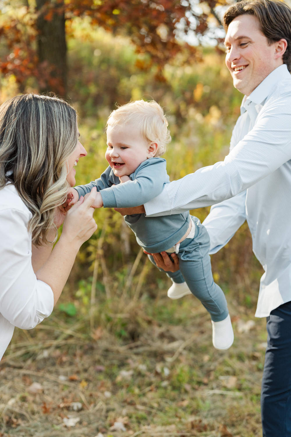 Smiling baby lifted between parents in golden field, joyful moment captured in natural Minneapolis photo places