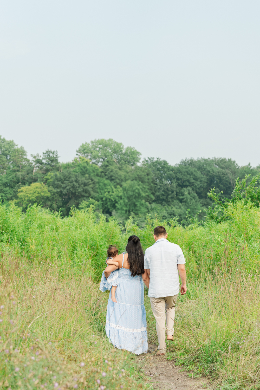 Family walking away together on a narrow path, surrounded by tall green grass in a quiet outdoor setting