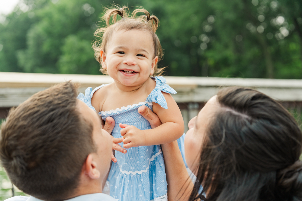 Smiling toddler lifted by parents outdoors, joyful moment captured in natural Minneapolis photo places setting