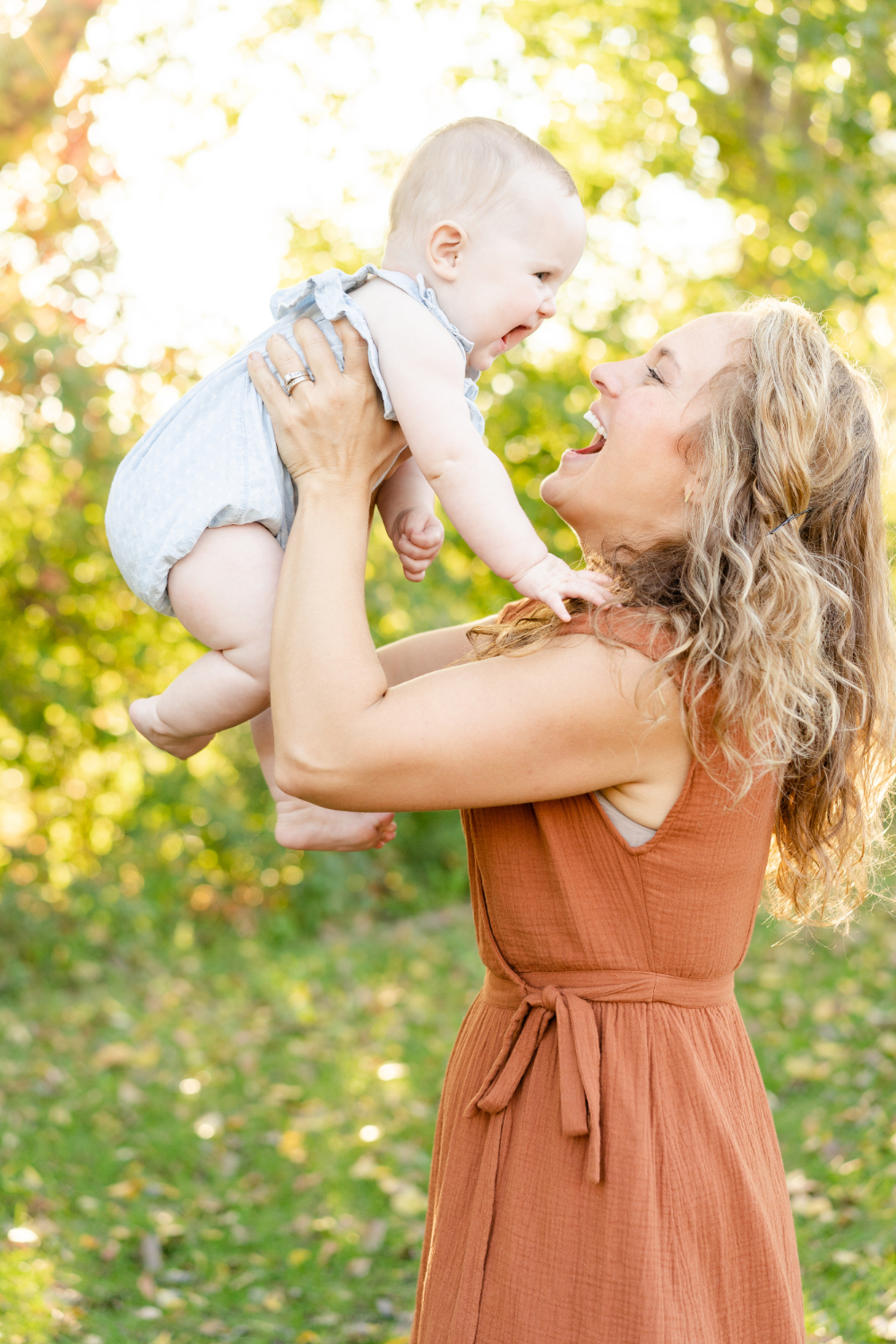 A joyful mother lifts her baby into the air as they share a playful moment surrounded by glowing sunlight. These golden hour photos capture the wonder of motherhood, highlighting laughter, connection, and the beautiful warmth of a Minnesota evening.