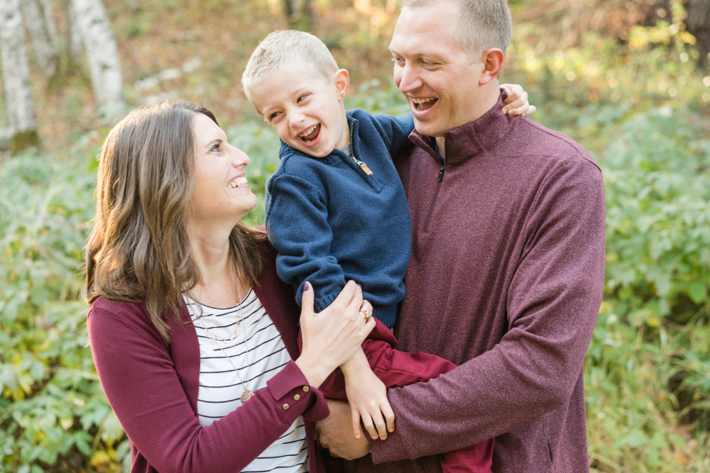 Parents laugh with their young son during a relaxed outdoor family photography session. The candid interaction and genuine expressions make these golden hour photos feel natural and full of joy, preserving a meaningful season of family life.
