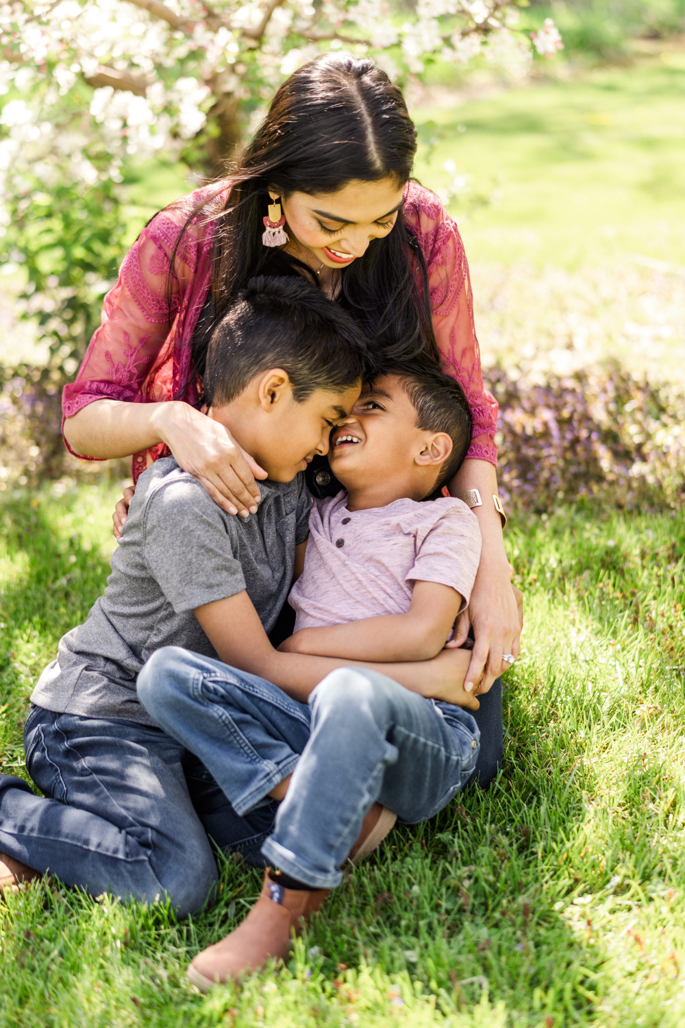 A mother embraces her two young sons beneath blooming trees during a spring family photography session. Their smiles and closeness reflect the importance of photography, capturing genuine affection and the beautiful bond that children will carry with them for years to come.