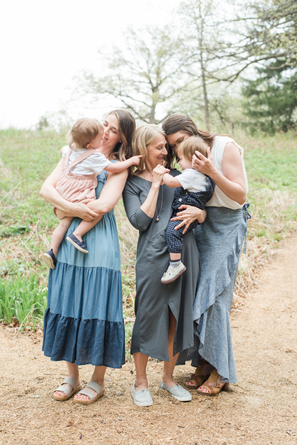 Three generations gather together along a nature trail, sharing hugs, smiles, and tender moments with young children. This heartfelt family portrait celebrates the importance of photography by preserving family connections, legacy, and the relationships that span generations.