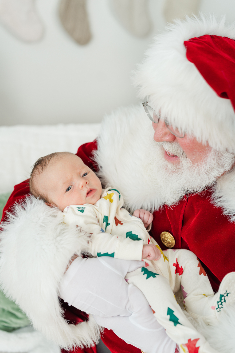 Baby wearing festive pajamas cuddled in Santa's arms during a holiday portrait session, showing adorable christmas photo outfits for little ones.